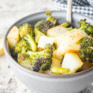 Roasted broccoli and potatoes in a bowl with a serving spoon.