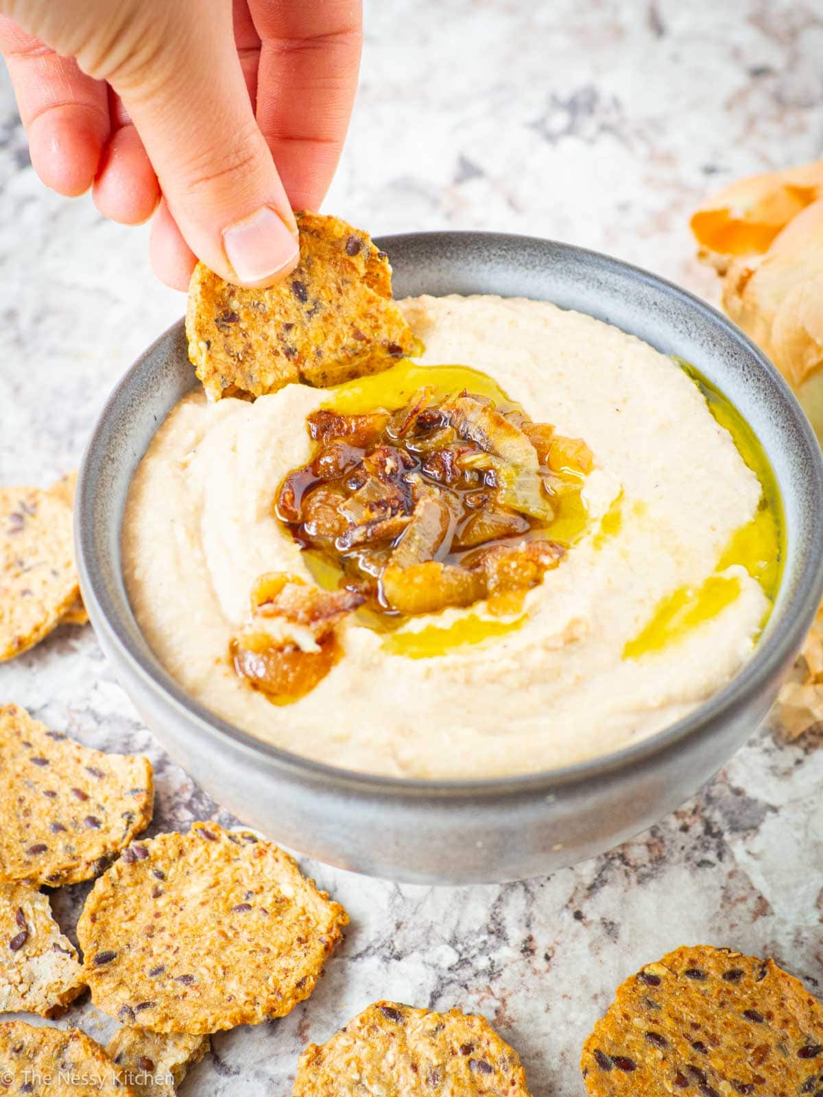 Hand dipping a cracker into a bowl of hummus.