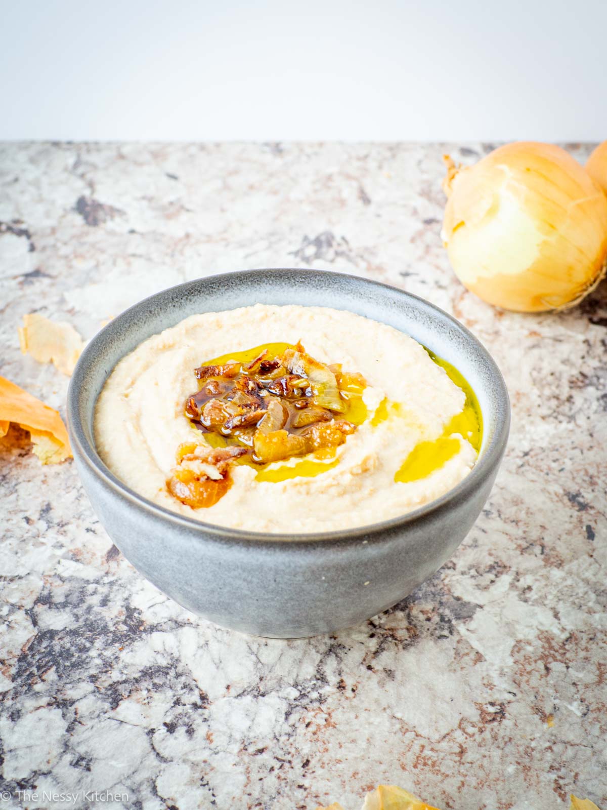 Hummus in a bowl with onions in the background.