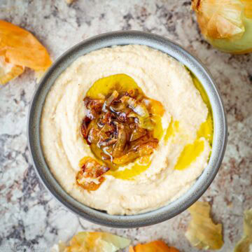 Hummus in a bowl topped with caramelized onions and a drizzle of olive oil.