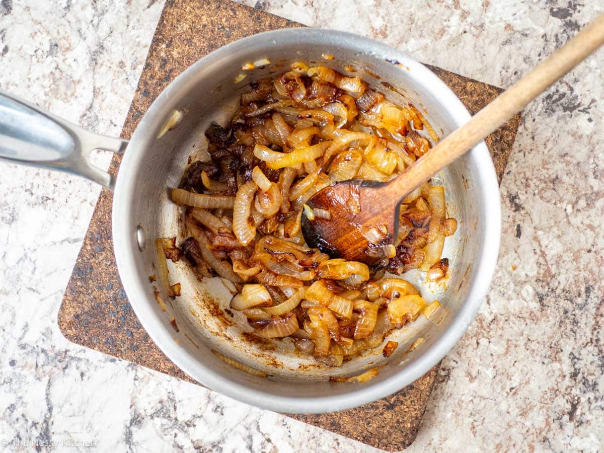 Cooked caramelized onions in a pan with a wooden spoon.