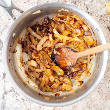 Caramelized onions in a saucepan with a wooden spoon.