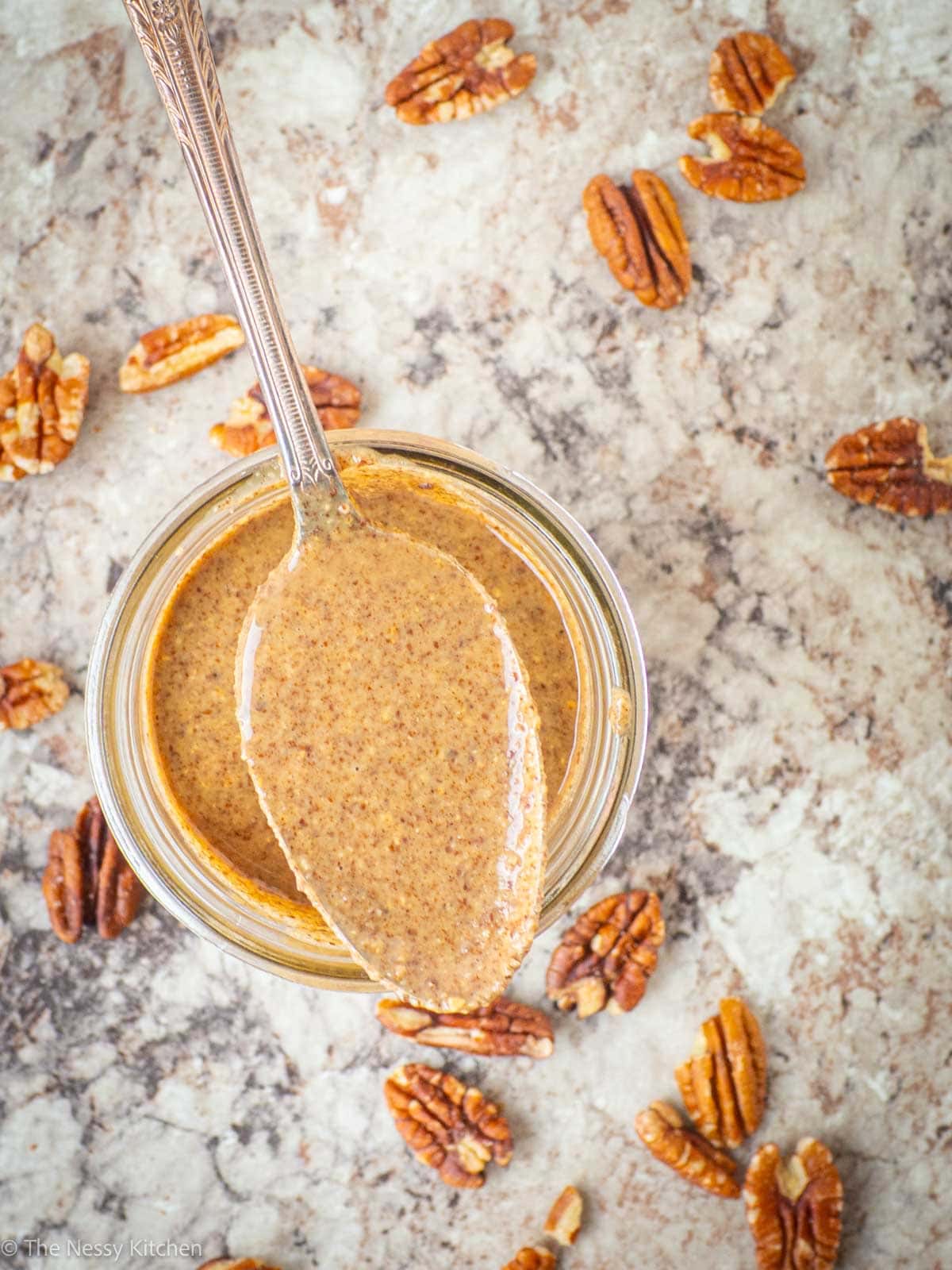 Spoonful of pecan butter sitting on a jar.