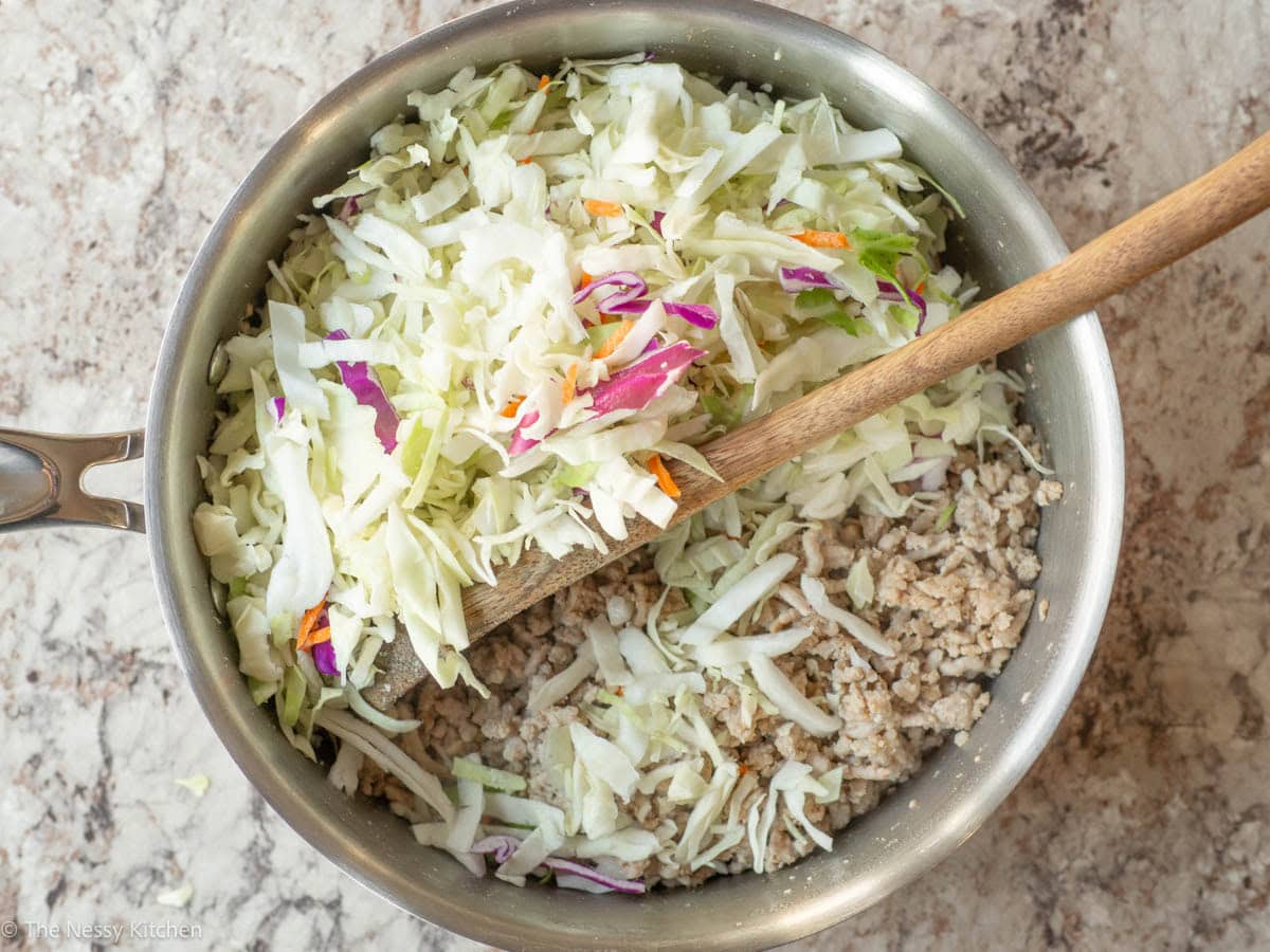 Coleslaw mix added to a skillet with ground pork.