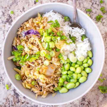 Egg roll in a bowl on a bed of rice and edamame.
