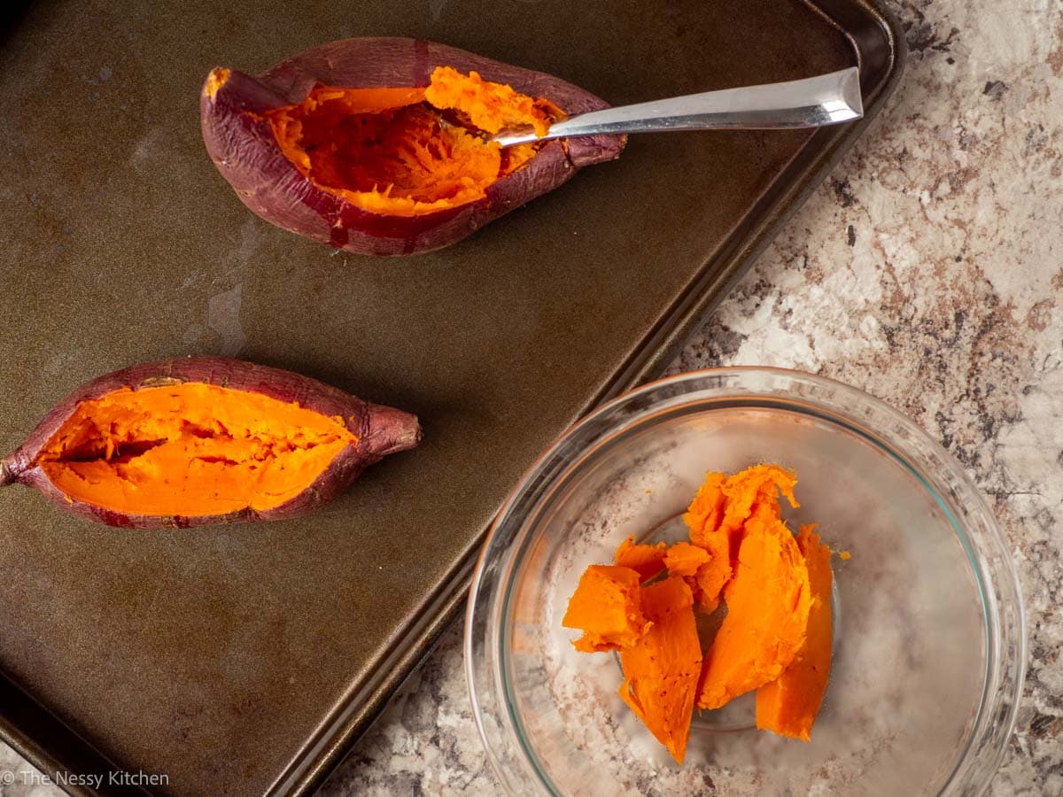 Sweet potatoes being hollowed out on a sheet pan.