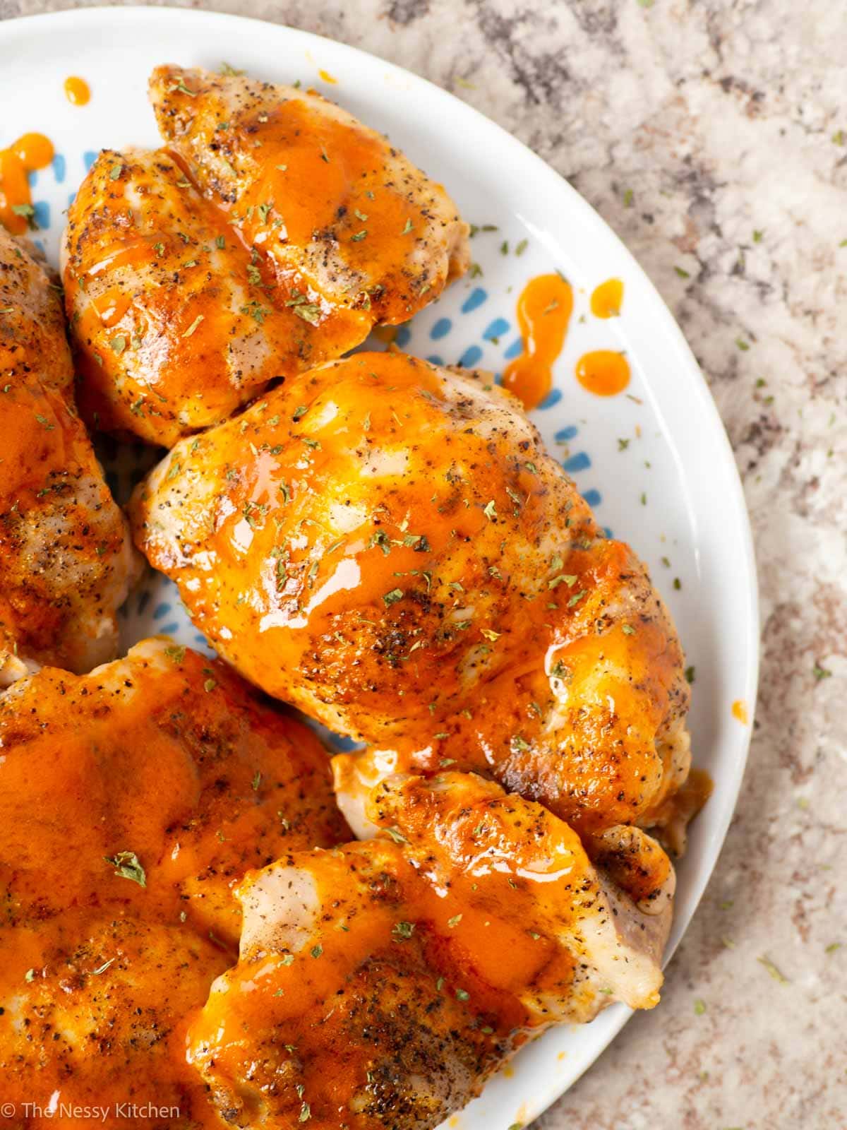 Plate of chicken thighs topped with Buffalo sauce.